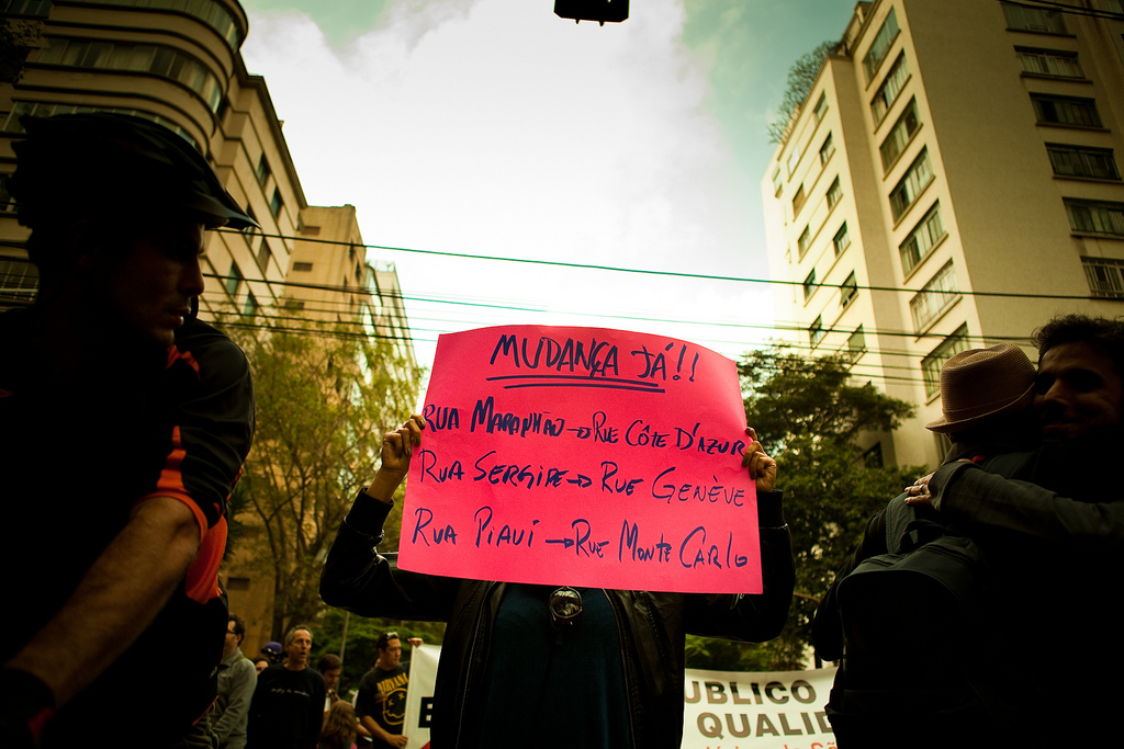 Mudança já! – Manifestante segura cartaz sugerindo a mudança dos nomes de ruas no bairro, substituindo os estados nordestinos por nomes em francês. Foto Luís Eduardo Catenacci, disponível no Flickr (CC BY-NC-SA 2.0)