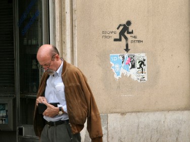 Grafiti numa rua de Lisboa, "Escapa do sistema" - lê-se na legenda: "Homem à procura de dinheiro para o bilhete". Foto de Trois Têtes (TT) no Flickr (CC BY-NC 2.0)