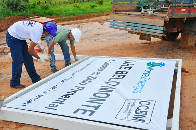 "Trabalhadores e a placa que demarca o local da obra da hidrelétrica de Belo Monte, na região do rio Xingu, no Pará - o sítio Pimental." Foto de Programa de Aceleração do Crescimento no Flickr (CC BY-NC-SA 2.0)